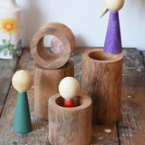 Papoose Toys wooden stacking tubes placed on a wooden surface with Goathe rainbow people placed on and inside the tubes.