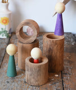 Papoose Toys wooden stacking tubes placed on a wooden surface with Goathe rainbow people placed on and inside the tubes.