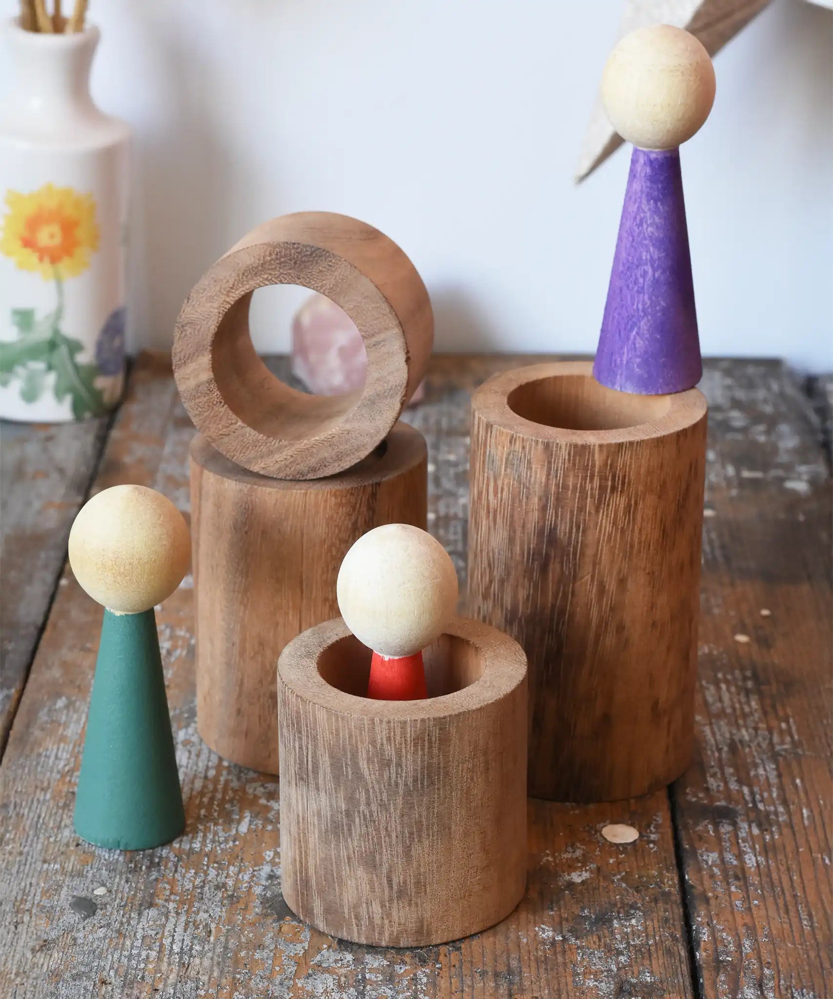 Papoose Toys wooden stacking tubes placed on a wooden surface with Goathe rainbow people placed on and inside the tubes.