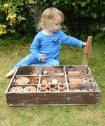 Child playing with the Papoose Toys wooden tinker tray school set outdoors.