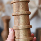 Large cylindrical spool with ridges from the Papoose Toys handmade wooden spool shape set in an adult's hand.