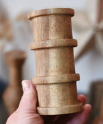 Large cylindrical spool with ridges from the Papoose Toys handmade wooden spool shape set in an adult's hand.
