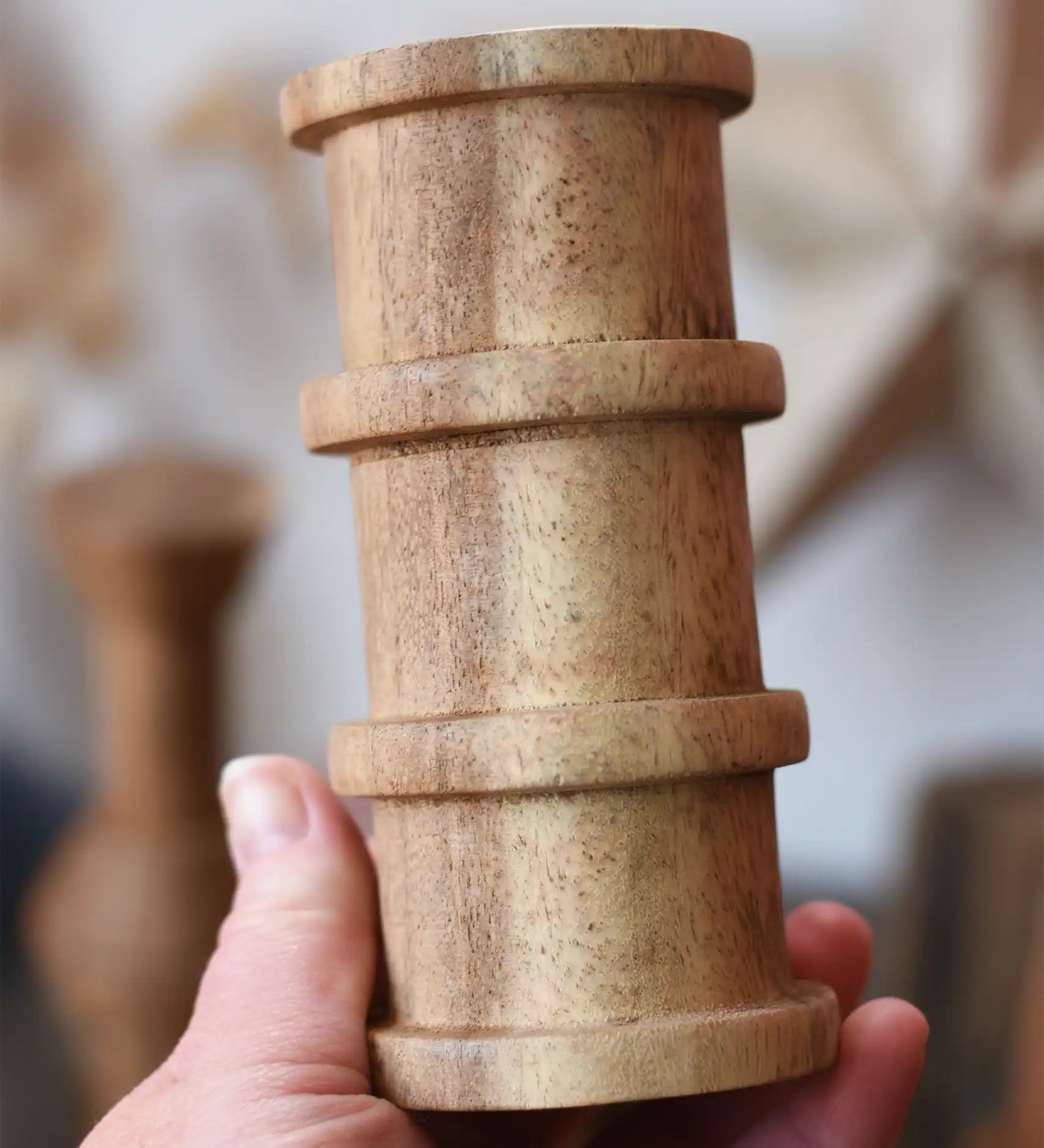 Large cylindrical spool with ridges from the Papoose Toys handmade wooden spool shape set in an adult's hand.