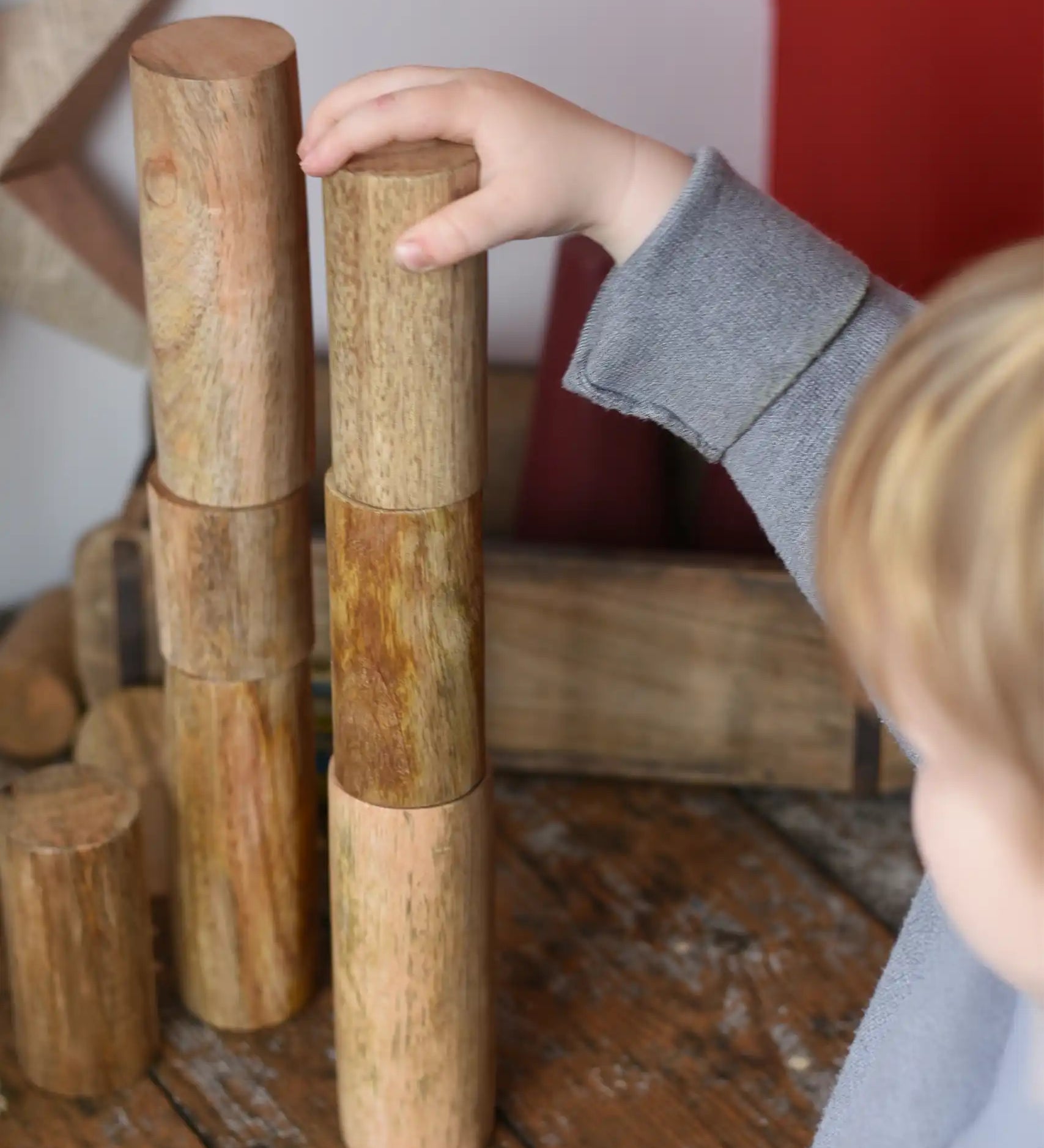 Papoose Toys wooden stacking trunks placed on a wooden desk. Child placing a trunk on top of a stack.