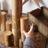 Papoose Toys wooden stacking trunks placed on a wooden desk. Child's hand reaching for a trunk.
