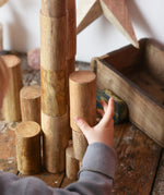 Papoose Toys wooden stacking trunks placed on a wooden desk. Child's hand reaching for a trunk.