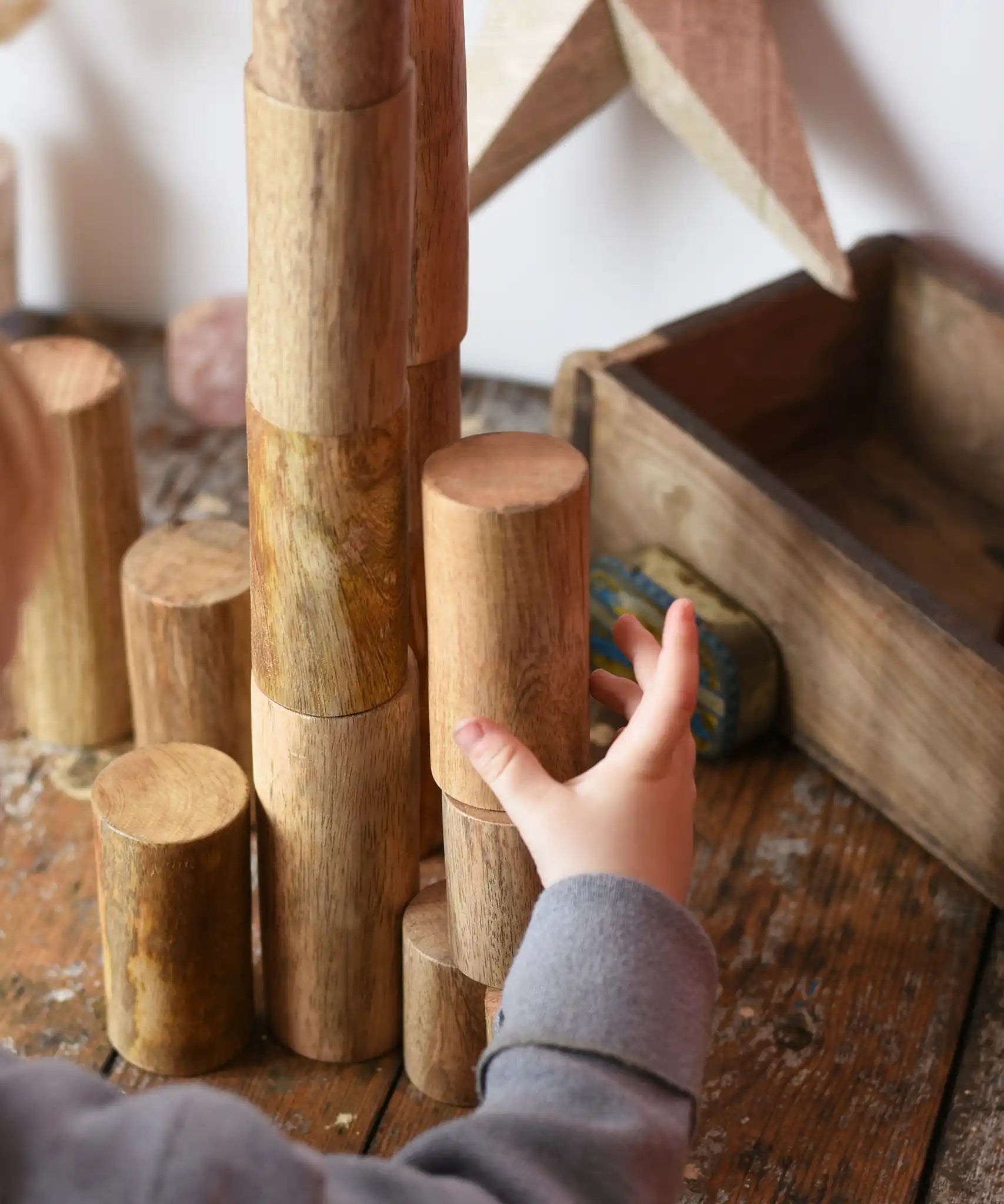 Papoose Toys wooden stacking trunks placed on a wooden desk. Child's hand reaching for a trunk.