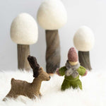 Papoose handmade felt reindeer figure and doll toy stood on a white fluffy blanket in front of 3 white Papoose trees