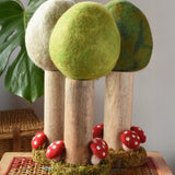 Papoose Toys Spring felt woodland tree placed on a rattan top stool with the Summer and Winter versions placed behind. 