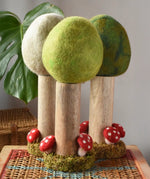 Papoose Toys Spring felt woodland tree placed on a rattan top stool with the Summer and Winter versions placed behind. 