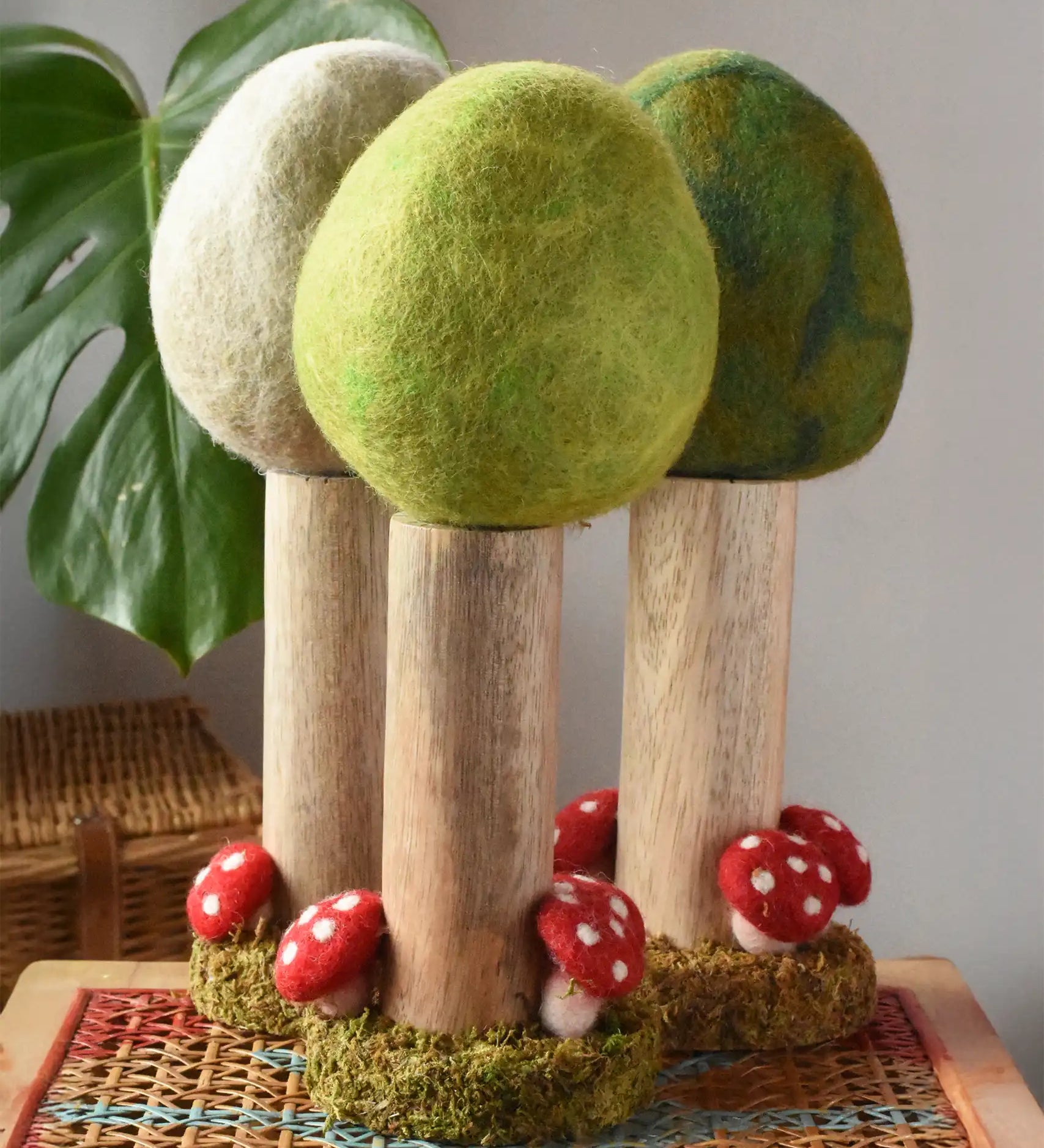 Papoose Toys Spring felt woodland tree placed on a rattan top stool with the Summer and Winter versions placed behind. 