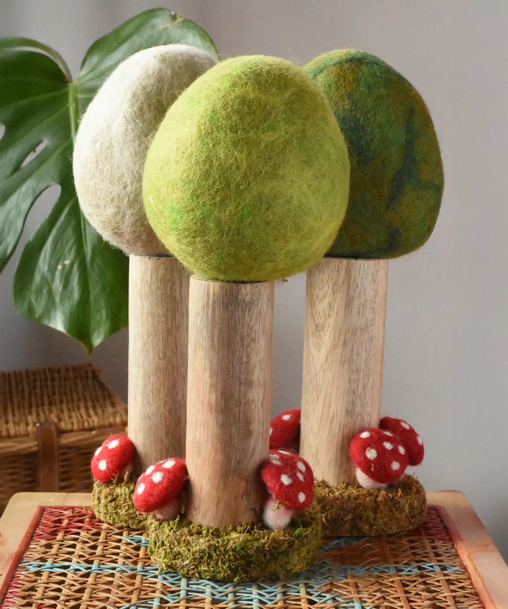 Papoose Toys Spring felt woodland tree placed on a rattan top stool with the Summer and Winter versions placed behind. 
