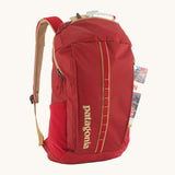 Patagonia Recycled Black Hole Backpack 25L in Touring Red with a map in the front zipper pocket and small essentials in the lid pocket on a cream background 