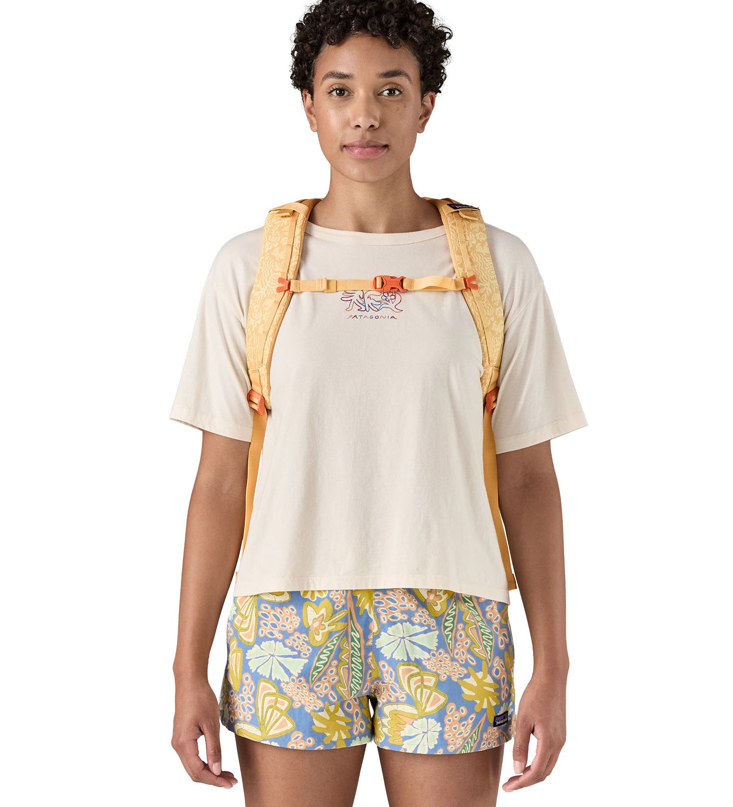 Patagonia 30L yellow refugio day backpack with a flower design  worn by an adult shoulder strap and clip detail