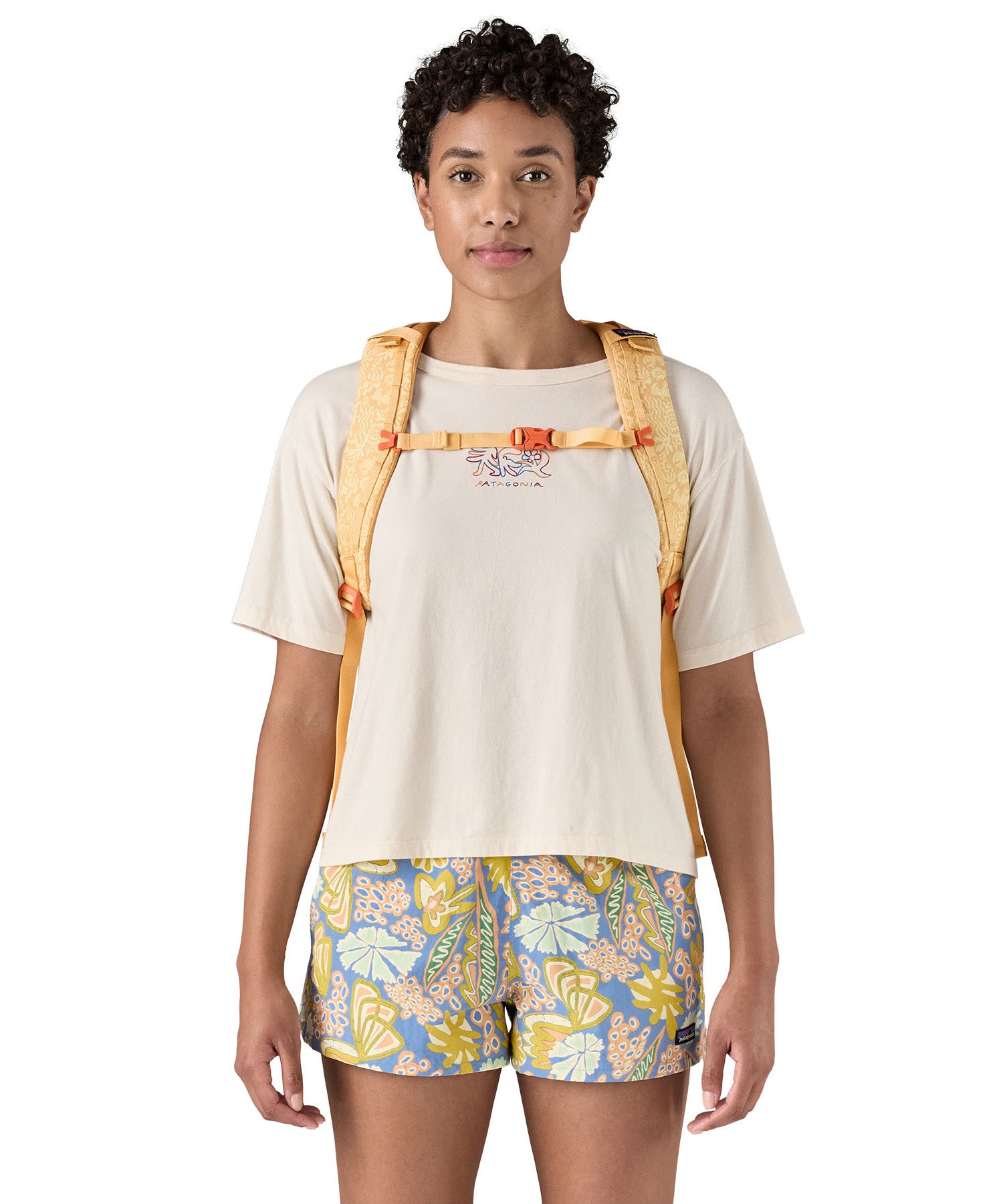 Patagonia 30L yellow refugio day backpack with a flower design  worn by an adult shoulder strap and clip detail