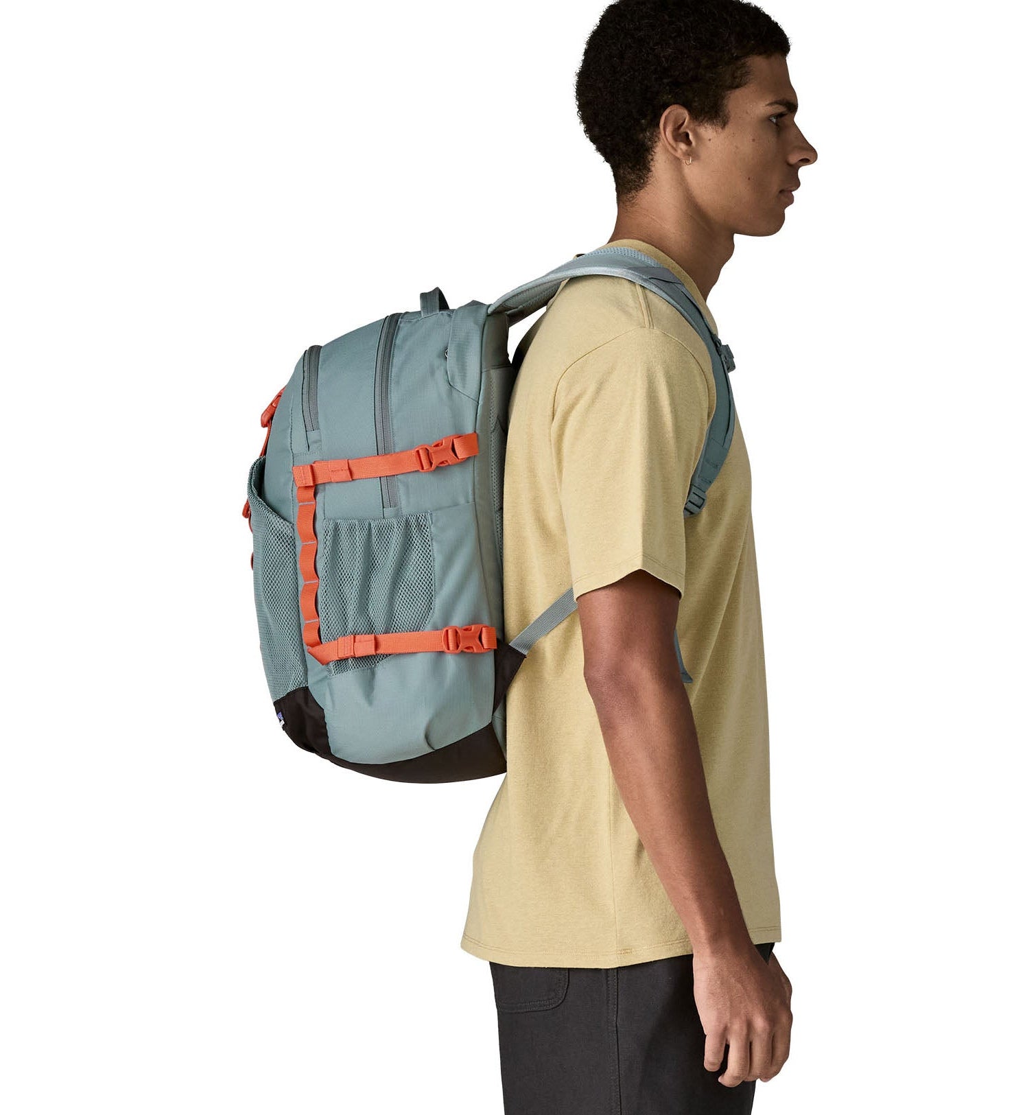 Person wearing a Patagonia 30L refugio backpack in blue sage with side bottle holder and orange gear loops and quick release buckles.