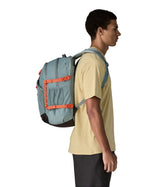 Person wearing a Patagonia 30L refugio backpack in blue sage with side bottle holder and orange gear loops and quick release buckles.