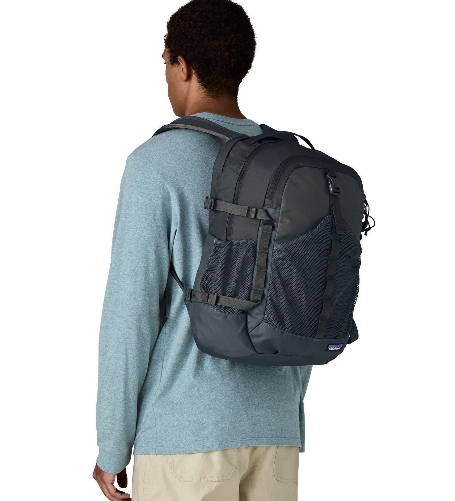 Person wearing a Patagonia 30L refugio backpack in smolder blue with side bottle holder and black gear loops and quick release buckles.
