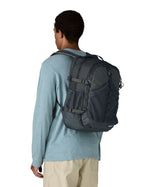 Person wearing a Patagonia 30L refugio backpack in smolder blue with side bottle holder and black gear loops and quick release buckles.