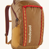 Patagonia 32L black hole packpack in talon gold. A 100% recycled polyester backpack in dark yellow and maroon detail. Features padded shoulder, side pockets for holding bottles and 2 compartments with cream branding on the front