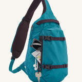 Patagonia Atom Sling 8L - Patchwork bag in Vessel Blue with items in the front pocket and a key clipped to the side of the zipper