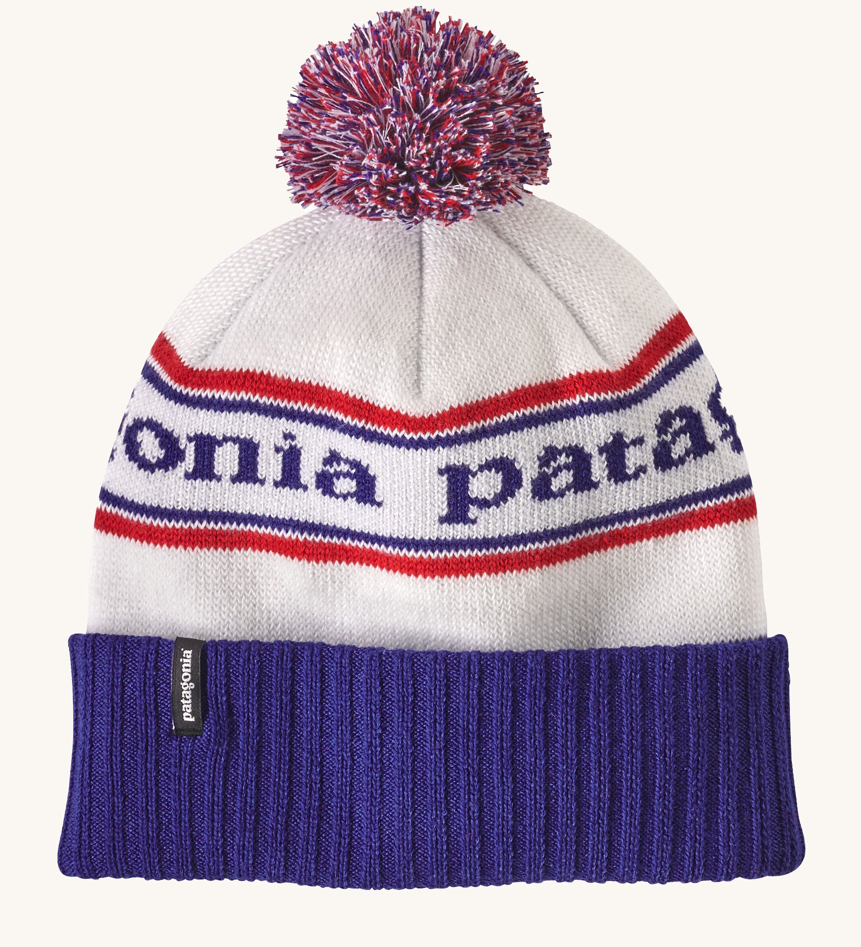 Patagonia adult beanie in white with a blue turn up ribbed brim. Features a red white and blue pom pom on top and the logo branding knitted into the hat. 