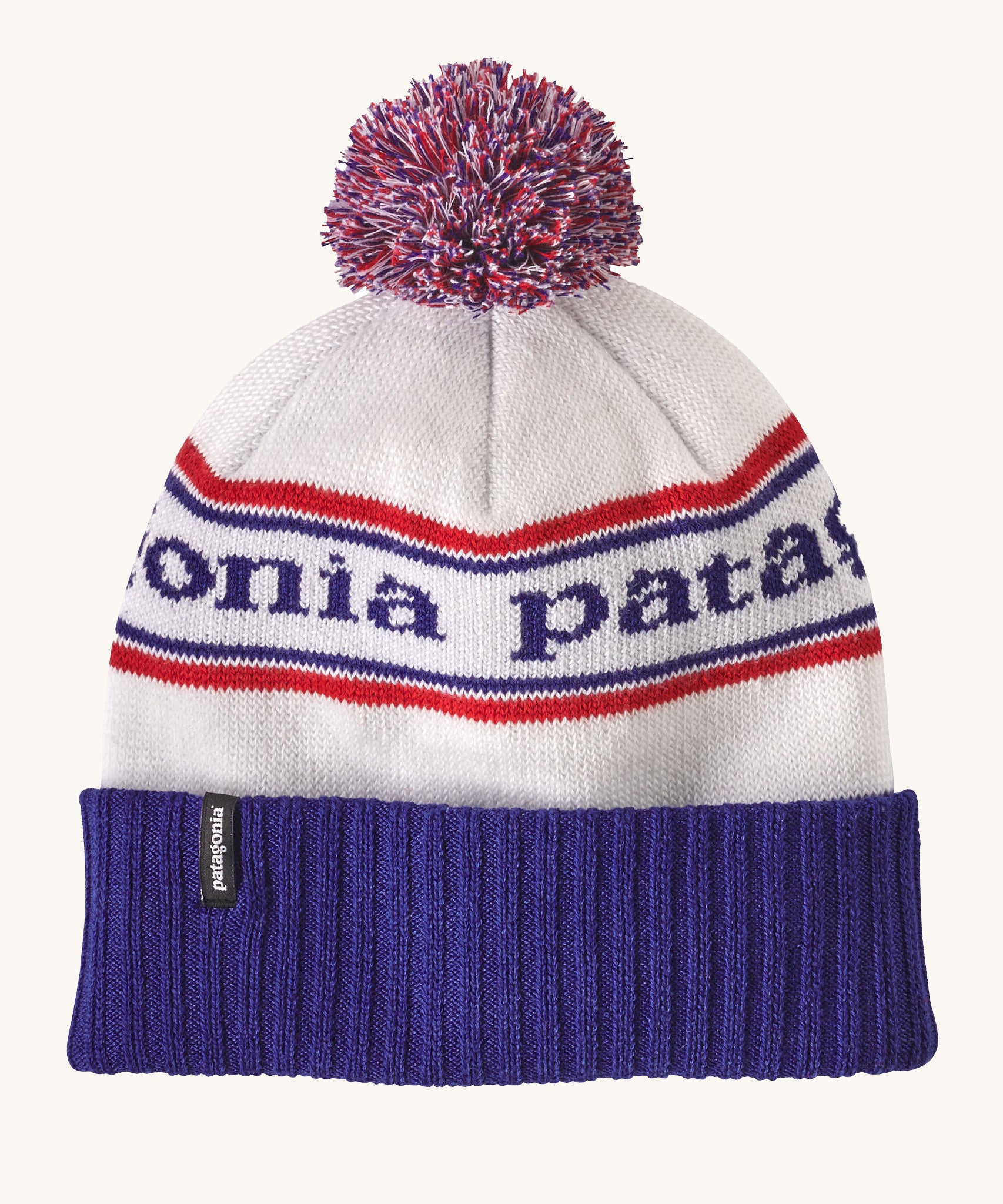 Patagonia adult beanie in white with a blue turn up ribbed brim. Features a red white and blue pom pom on top and the logo branding knitted into the hat. 
