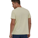 A man wearing a Patagonia Adult Fitz Roy Icon Responsibili-Tee in a Birch White colour stood in front of a plain background. The man is facing away from the camera showing the back of the t-shirt which is plain. 