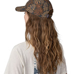 A woman wearing a Patagonia Adult P-6 Label Trad Cap in a Sun Wave design stood in front of a plain background. The woman is facing away from the camera showing the back of the cap. 