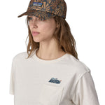 A woman wearing a Patagonia Adult P-6 Label Trad Cap in a Sun Wave design stood in front of a plain background.