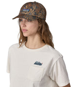 A woman wearing a Patagonia Adult P-6 Label Trad Cap in a Sun Wave design stood in front of a plain background.