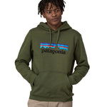 A man wearing a Patagonia Adult P-6 Logo Uprisal Hoody in a Torrey Pine Green colour, he is stood in front of a plain background.