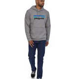 A man wearing a Patagonia Adult P-6 Logo Uprisal Hoody in a Gravel Heather grey colour stood in front of a plain background. 