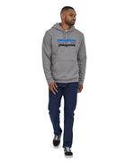 A man wearing a Patagonia Adult P-6 Logo Uprisal Hoody in a Gravel Heather grey colour stood in front of a plain background. 