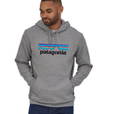 A man wearing a Patagonia Adult P-6 Logo Uprisal Hoody in a Gravel Heather grey colour stood in front of a plain background. 