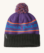 A black and purple adult Patagonia beanie hat with a orange strip and light blue branding on a cream background