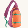 Patagonia atom cross body 8L sling bag in faded magenta with an orange front pocket and handle and mint gear straps and buckles.