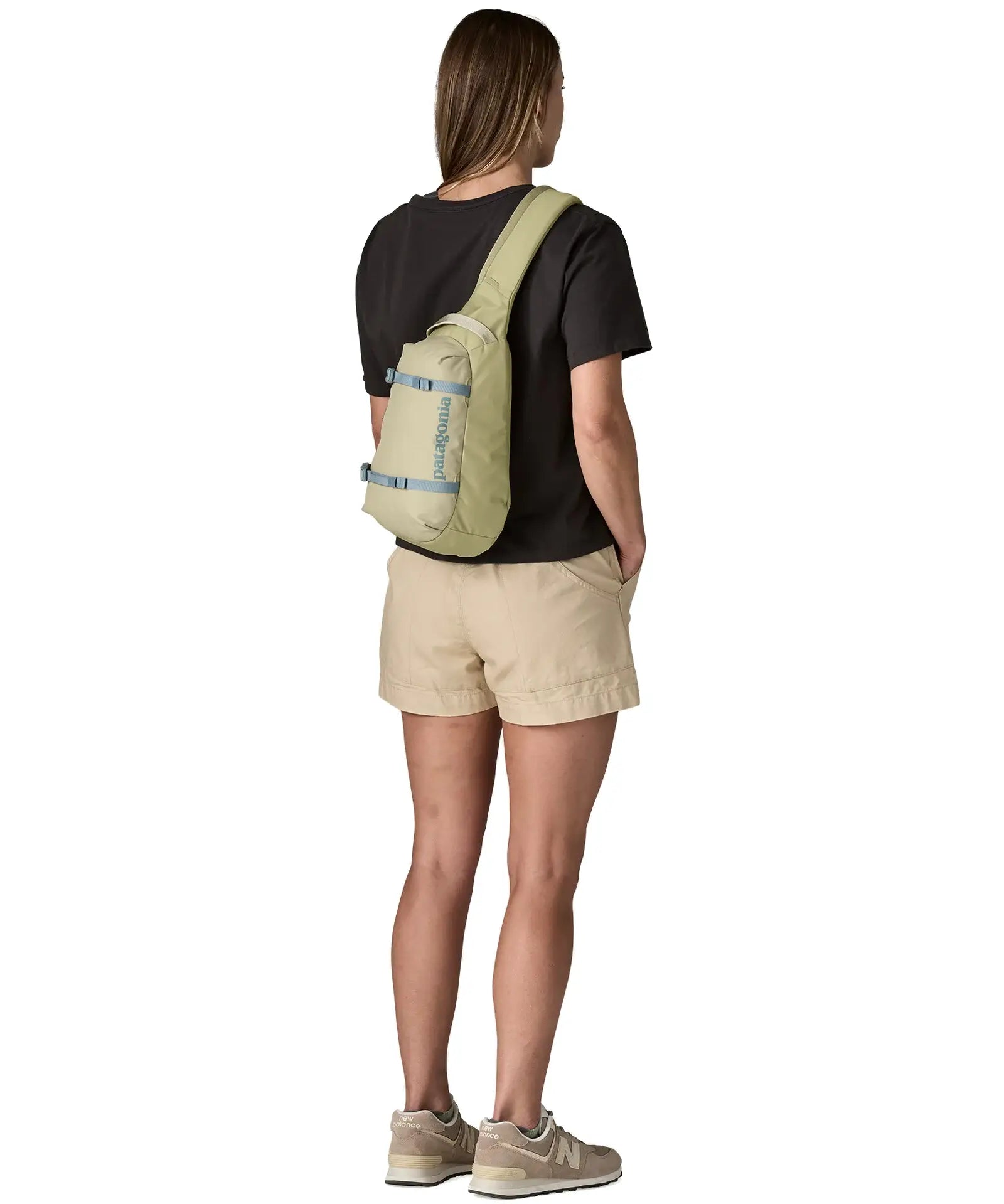 Back woman wearing the Patagonia atom cross body 8L sling bag in pale green over the shoulder showing grey gear buckles