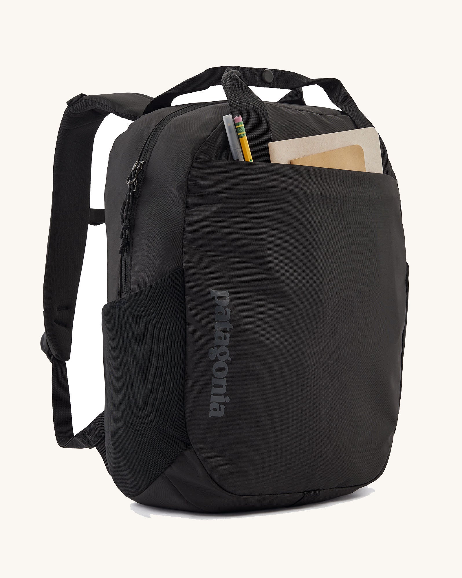 Patagonia atom 20 litre black tote bag backpack shown with stationery in the front pocket.