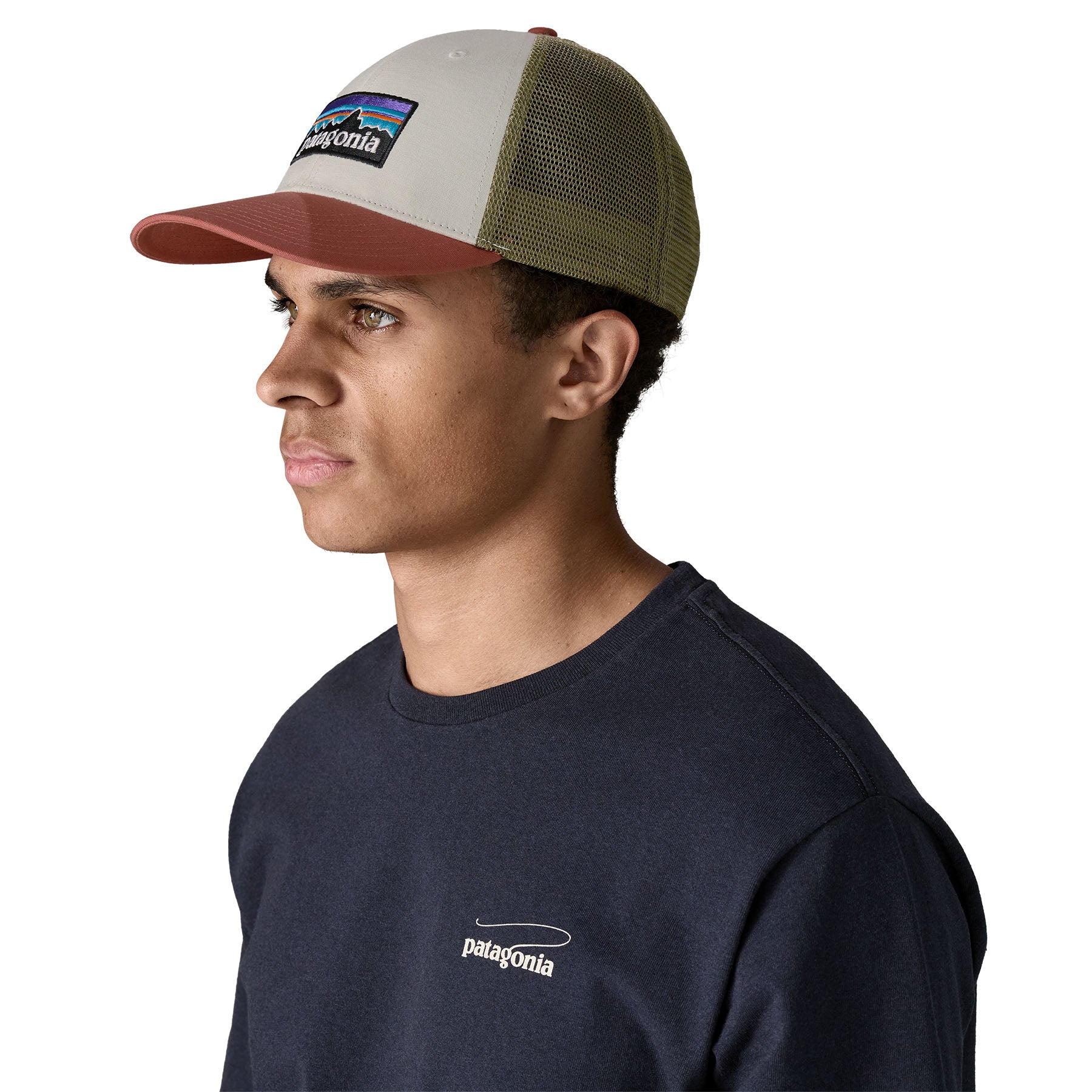 A man wearing the Patagonia adult birch white hat. A trucker style cap with a low profile in white colour and features a khaki mesh back with a coral brim and logo embroidery on the front panel available at Babipur.
