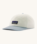 Patagonia trad cap in birch white and light blue on a cream background.