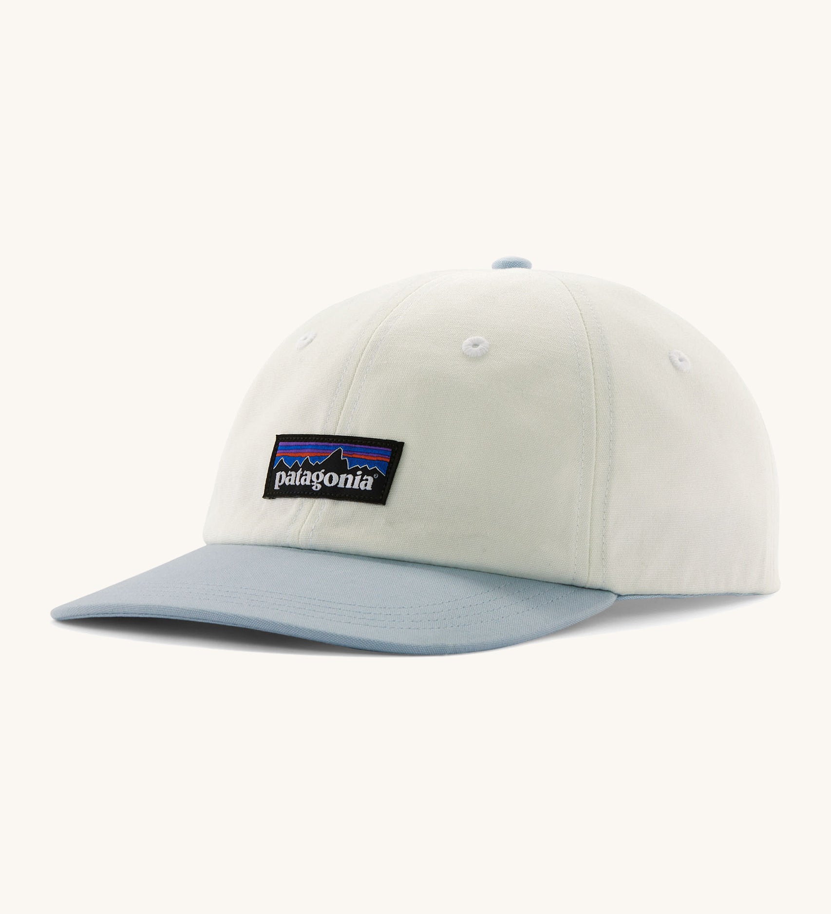 Patagonia trad cap in birch white and light blue on a cream background.
