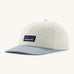 Patagonia trad cap in birch white and light blue on a cream background.
