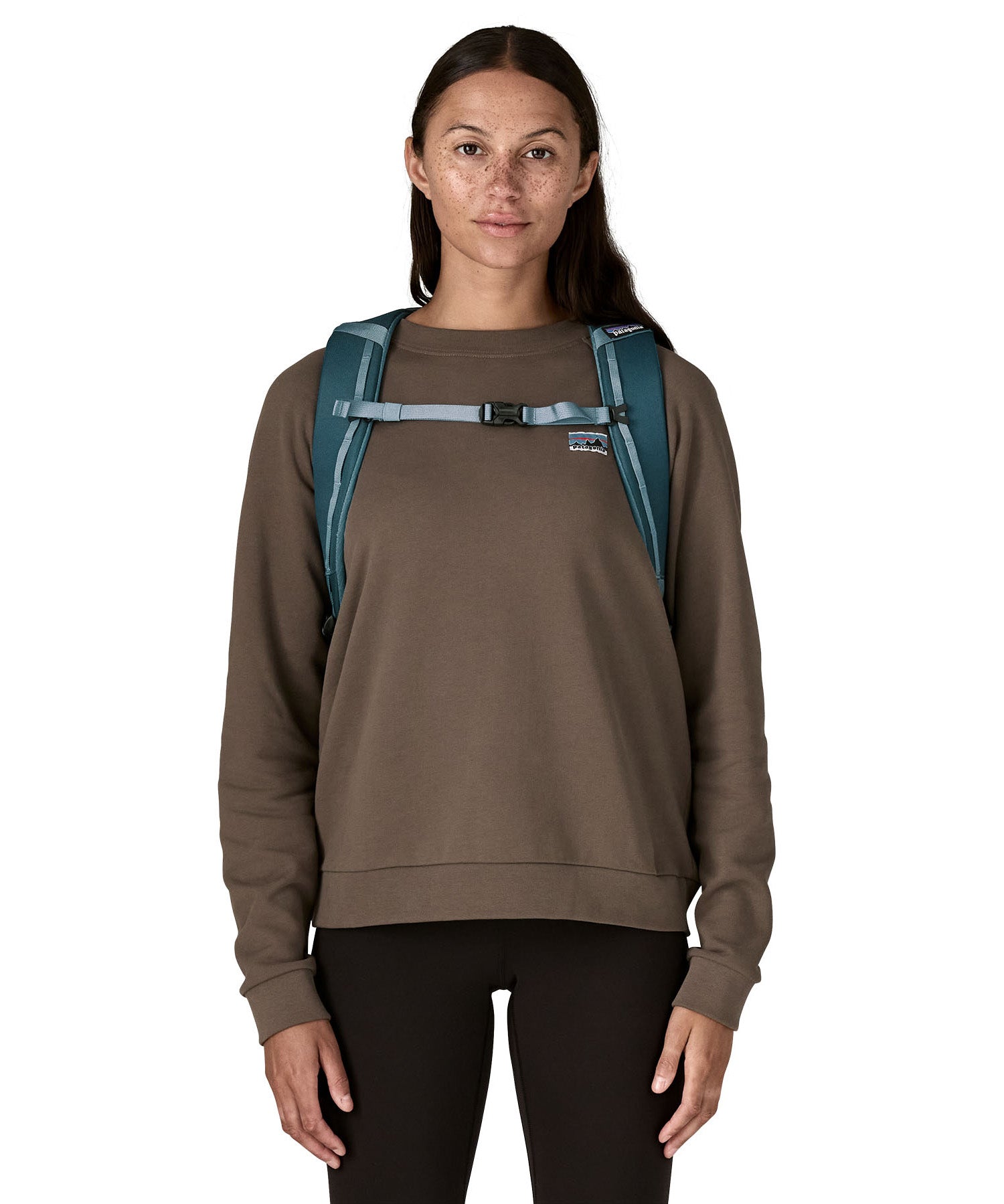Front view of a woman wearing the Patagonia Black Hole Backpack 25L in Tidal Teal, to showcase the chest straps that keep the rucksack secure on adventures. 