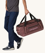 A person holding a 55L Patagonia Black Hole Duffel bag.