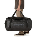 A man holding the large 100 litre capacity Patagonia Black Hole Duffel Luggage Bag, in monochrome all black, by the handles. 
