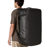 A man wearing the large 100 litre capacity Patagonia Black Hole Duffel Luggage Bag, in monochrome all black., on his back as a backpack. 