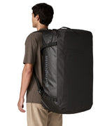 A man wearing the large 100 litre capacity Patagonia Black Hole Duffel Luggage Bag, in monochrome all black., on his back as a backpack. 