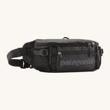 Patagonia black hole waist 5L pack in black on black. A 100% recycled nylon pack in black with black detail. Features 2 compartments with mesh side pockets and a buckle fastener 