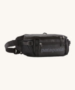 Patagonia black hole waist 5L pack in black on black. A 100% recycled nylon pack in black with black detail. Features 2 compartments with mesh side pockets and a buckle fastener 